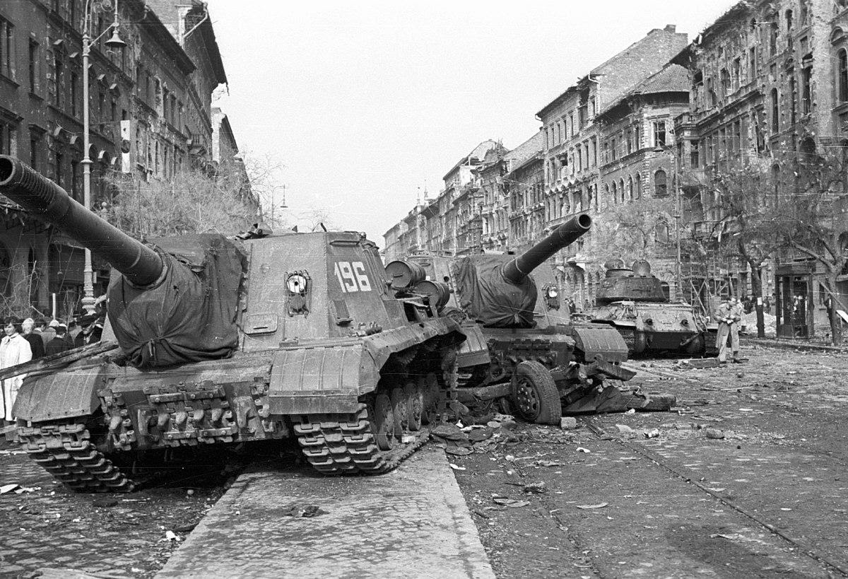 Two Soviet ISU-152 self-propelled guns in Budapest with an abandoned T-34/85 tank in the background Wikimedia Commons